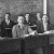 Eight male students sitting at their desks look to camera for a photo of the Secunda Class of 1934