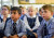 Two boys sit in the foreground listening to the teacher with other students sitting behind