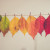 A series of seven leaves suspended from a wire, showing the autumn colour change from green through yellow and orange to red