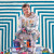 Artist Dave Court sits atop a pile of paint tins in front of a striking, striped background